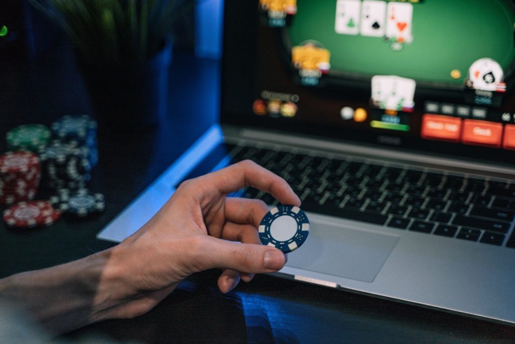 Hand with poker chip and laptop in the background